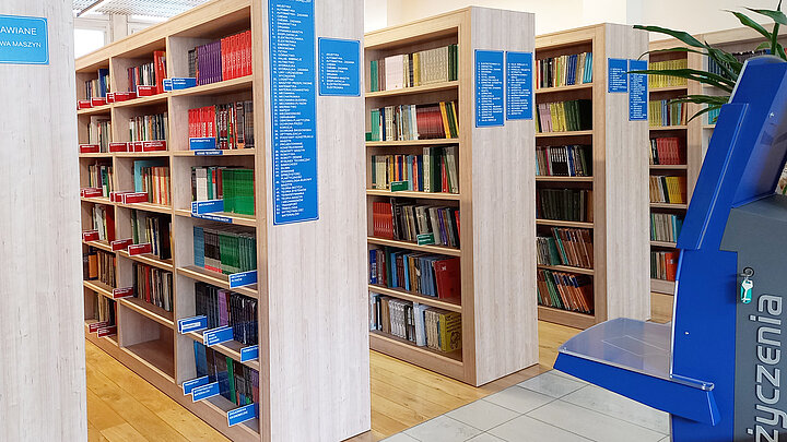 Zdjęcie podłużnych drewnianych regałow bibliotecznych z książkami.