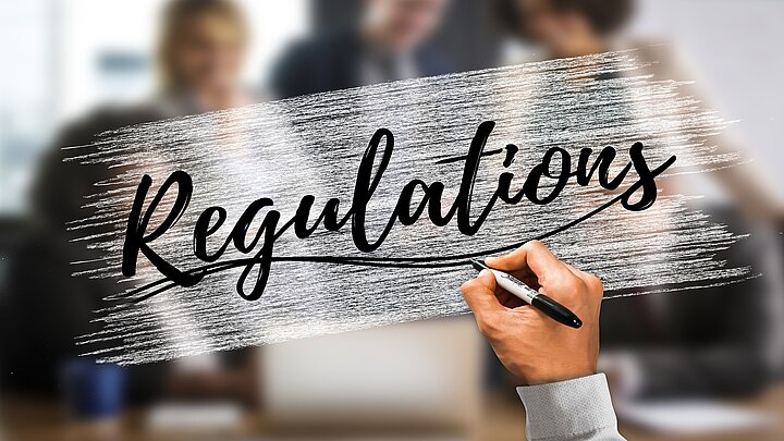 na szybie ręka pisze słowo regulations, za szybą zamazane postacie